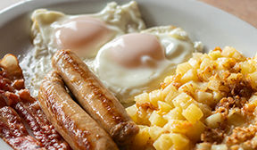 Breakfast plate of bacon, sausage, eggs and hashbrown homefries.