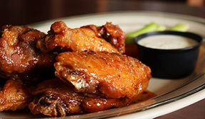 Close up view of saucey chicken wings with ranch dressing in background.