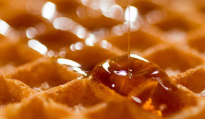 Close up of a few waffle squares with syrup pouring carefully and overflowing one square.
