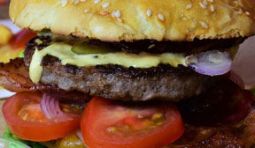 Tomato, mayo spilling out of a juciy prime rib beef hamburger 