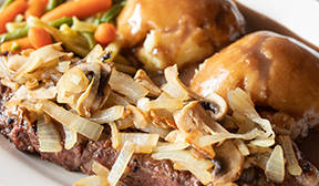 Steak covered with onions and mushrooms with mashpotatos covered in gravy and mixed vegetables on a plate.